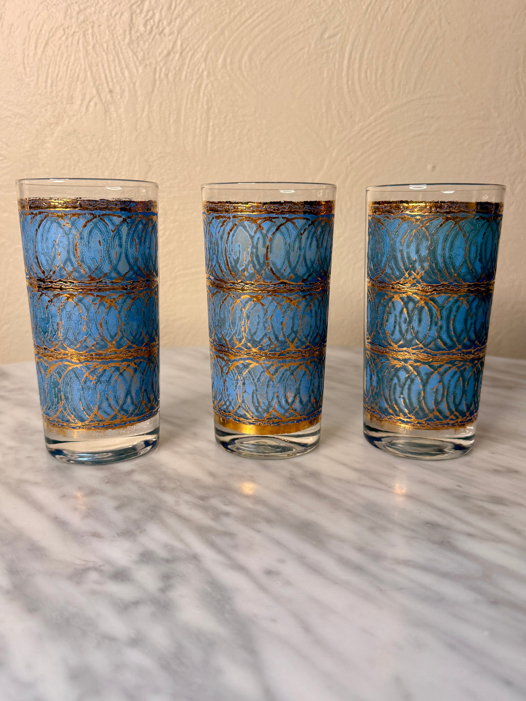 Three vintage Georges Briard highball glasses with blue interlocking oval patterns and 22-karat gold detailing.