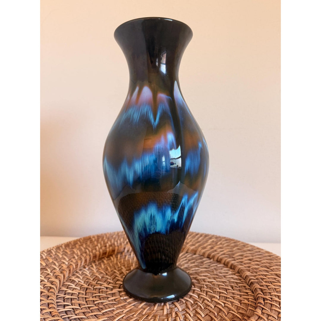 Vintage Rainbow Ceramics vase with blue, teal and copper drip glaze over black, an elongated rounded body, flared opening and pedestal base.