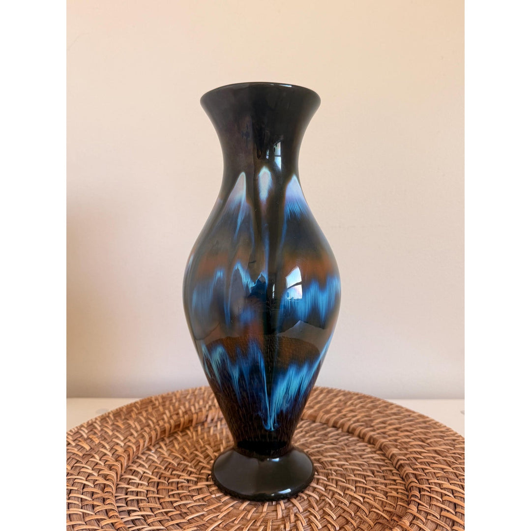 Vintage Rainbow Ceramics vase with blue, teal and copper drip glaze over black, an elongated rounded body, flared opening and pedestal base.
