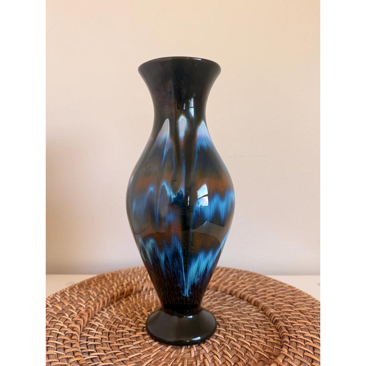 Vintage Rainbow Ceramics vase with blue, teal and copper drip glaze over black, an elongated rounded body, flared opening and pedestal base.